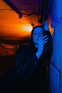 a woman leaning up against a wall talking on a cell phone with blue light in the background