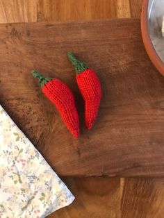 two crocheted strawberries sitting on top of a wooden cutting board next to a bowl