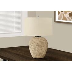 a table lamp with a white shade on it and a brown wooden table in front of a window