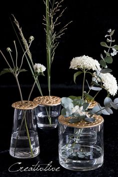 three clear vases with flowers and greenery in them