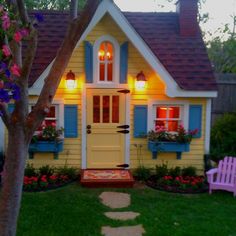 a small yellow house with blue shutters and flowers in the window boxes on either side