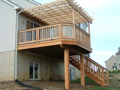 a wooden deck on the side of a house with stairs leading up to an upper level