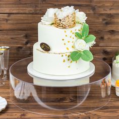 a white wedding cake with flowers and a gold crown on top is sitting on a clear platter