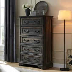 an old chest of drawers in a room with a lamp and flowers on the table