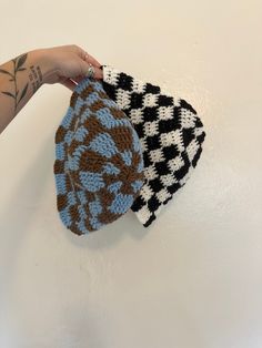 a hand is holding two knitted hats on a white surface, one blue and the other brown