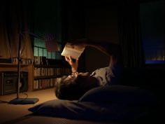 a man laying in bed with his head on the pillow while holding a lamp above his head