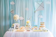 a table topped with lots of cakes and cupcakes next to a wall covered in clouds