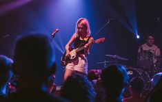 a woman playing guitar in front of a crowd at a music concert with other people