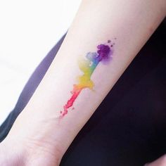 a woman's arm with a colorful watercolor tattoo design on the left wrist