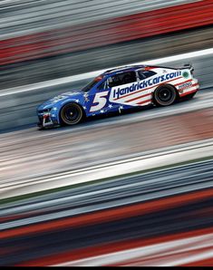 a race car driving on a track with red, white and blue stripes behind it