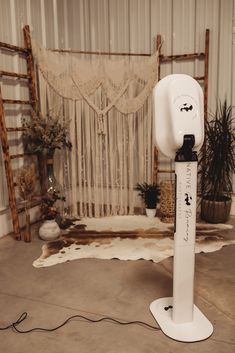 a white object with writing on it sitting in front of a curtain and potted plant