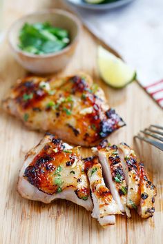 two pieces of chicken on a cutting board with a knife and fork next to it