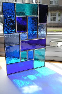 a blue and purple stained glass block hanging from a window sill in front of a building