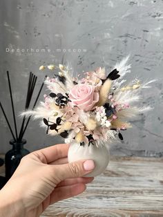 a hand holding a vase with flowers and feathers