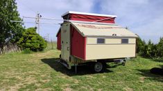 a small red and white trailer sitting on top of a grass covered field