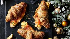 croissants with salmon and cheese are on a black tray surrounded by christmas decorations