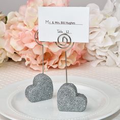 two heart shaped silver glitter cake toppers on a white plate with flowers in the background