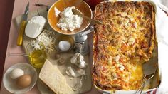 a casserole dish with cheese, eggs and other ingredients on a table next to utensils