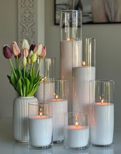 a vase filled with lots of white candles next to some pink and yellow tulips