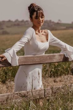 a woman in white dress leaning on a wooden fence