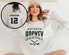 a woman sitting on top of a bed wearing a white sweatshirt with hockey written on it