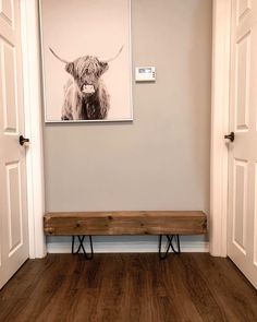 a wooden bench sitting in front of a white wall with a cow photo on it