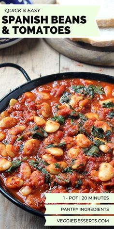 a pan filled with beans and spinach on top of a wooden table next to bread