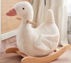 a white stuffed duck sitting on top of a wooden rocking toy