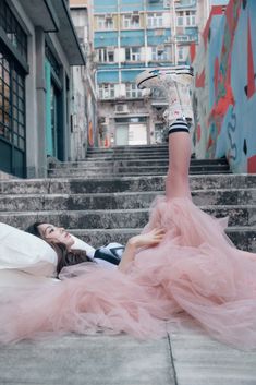 a woman laying on the ground with her legs up in front of her head, wearing a pink dress and high heels