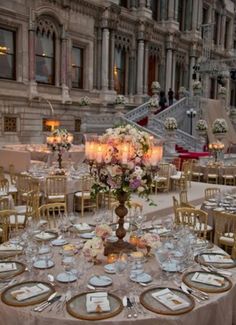 a table set up for a formal dinner in front of a building with candles and flowers on it