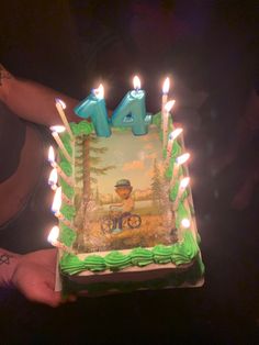 a person holding a birthday cake with candles in the shape of a man riding a bike