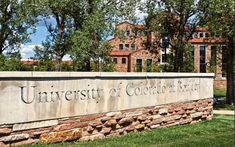 the university of colorado sign is shown in front of some trees and grass on a sunny day