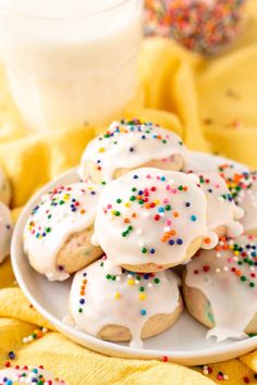 white frosted cookies with sprinkles on a plate next to a glass of milk