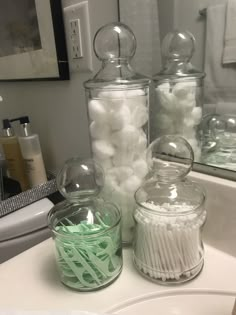 three glass jars filled with white and green candy sitting on top of a bathroom sink