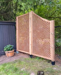 a wooden privacy screen next to a potted plant in a yard with trees and fence behind it