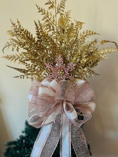 a vase filled with gold and silver flowers on top of a wooden table next to a christmas tree