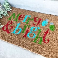 a merry and bright door mat sitting on the ground next to a potted plant