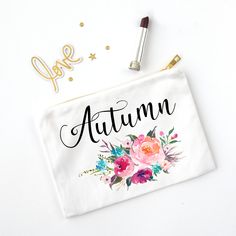 a white pouch with the word autumn written on it next to lipstick and gold confetti