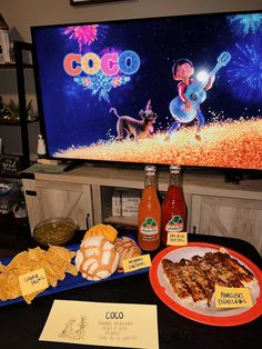 a table topped with food and drinks next to a flat screen tv displaying coco's fireworks