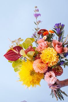 a person holding a bouquet of flowers in their hand with blue sky in the background