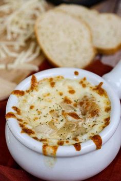 a white bowl filled with food next to slices of bread on top of a table