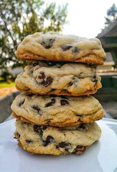 three chocolate chip cookies stacked on top of each other in front of a house and trees