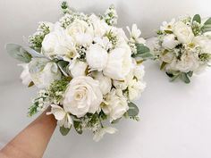 two bridal bouquets with white flowers are being held by someone's hand