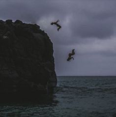 two people jumping off rocks into the ocean at night with dark clouds in the background