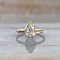 a yellow gold ring with a pear shaped diamond in the center on a wooden surface