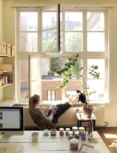 a woman sitting on a window sill with a cat in her lap looking out the window