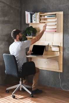 a man sitting at a desk with a laptop computer in front of him and holding his hand up to the wall