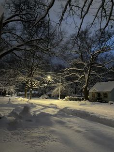 a snow covered street with houses and trees in the background at night time, during winter