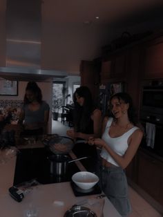 three women standing in a kitchen preparing food on the stove top, and one woman is smiling