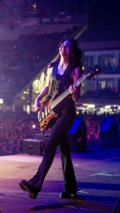 a woman holding a guitar while standing on top of a stage with an audience in the background